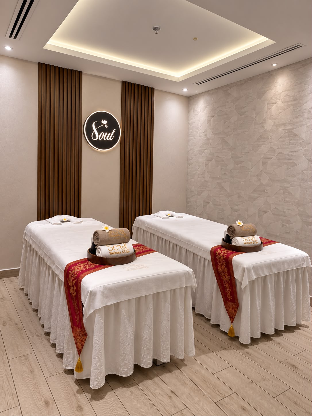 Treatment suite with two dressed massage tables, white linen, and a red-gold runner.